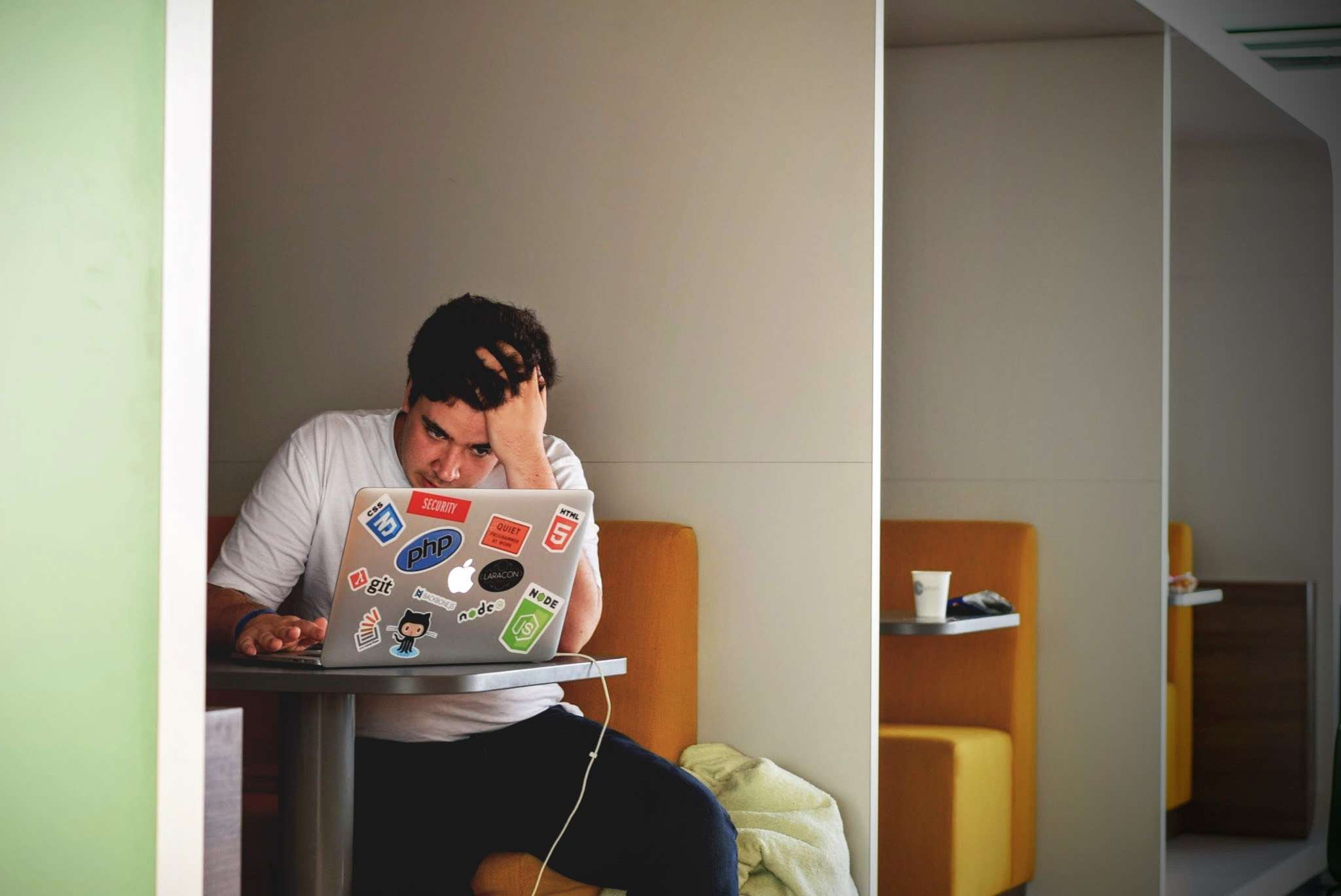young man sitting at a study desk, staring at a computer screen, with his head resting on his hand.